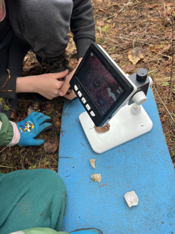 Child using a microscope to explore nature during outdoor learning at Roots To Sky Forest School in Nelson BC